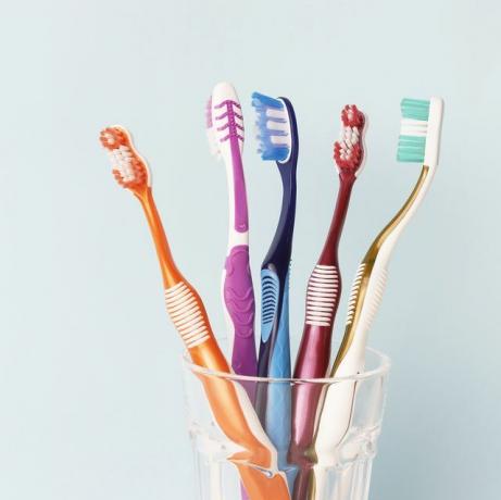 Πολύχρωμες οδοντόβουρτσες σε γυάλινο κύπελλο, μπλε φόντο